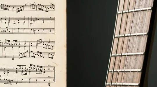 A close-up view showing the intersection of classical sheet music with rock guitar strings in natural studio lighting