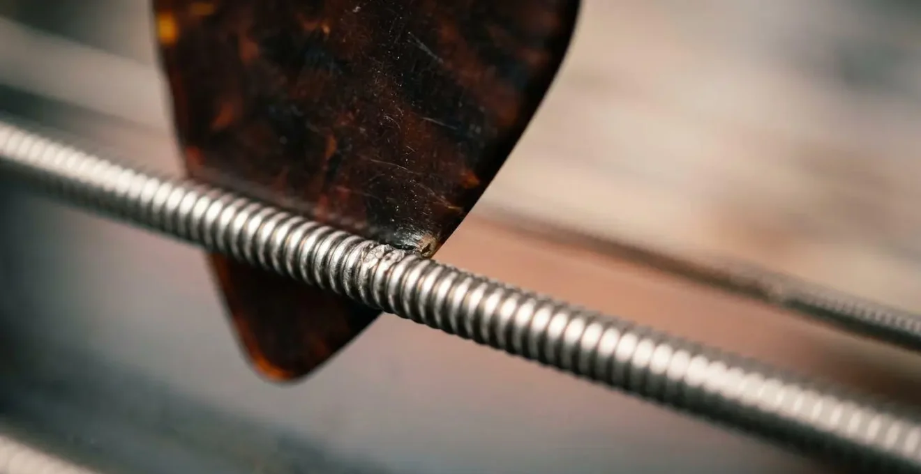 Extreme close-up of bass guitar pick striking string showing transient moment