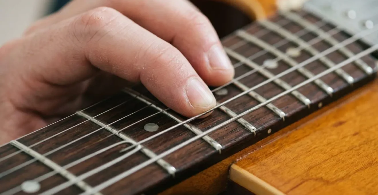Extreme close-up of guitar strings and frets with fingers forming a chord position, showing tactile wood grain and metal fret texture