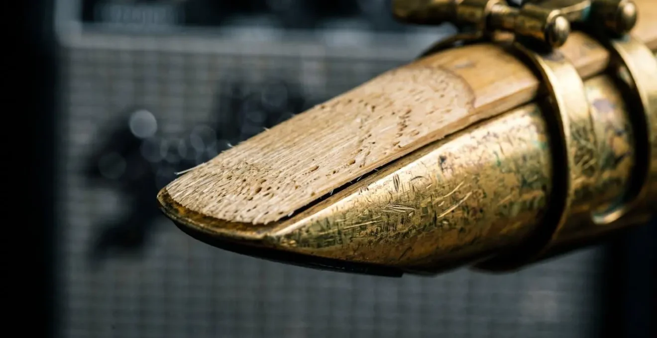 Close-up macro shot of a saxophone mouthpiece and reed with electric guitar amplifier texture in background